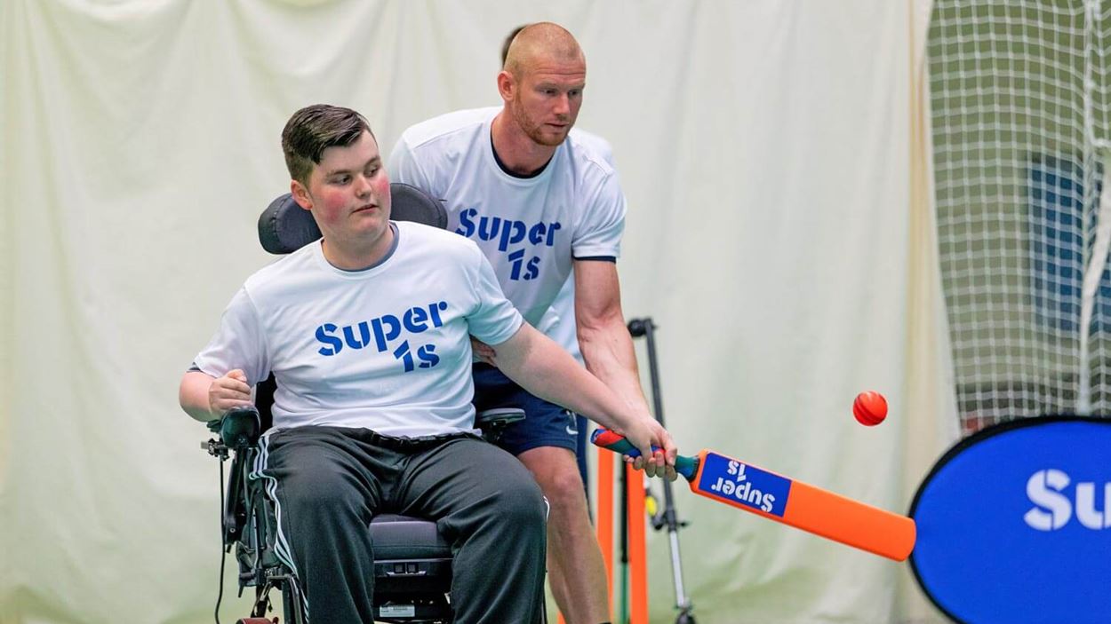 Player in wheelchair being helped as he hits a ball