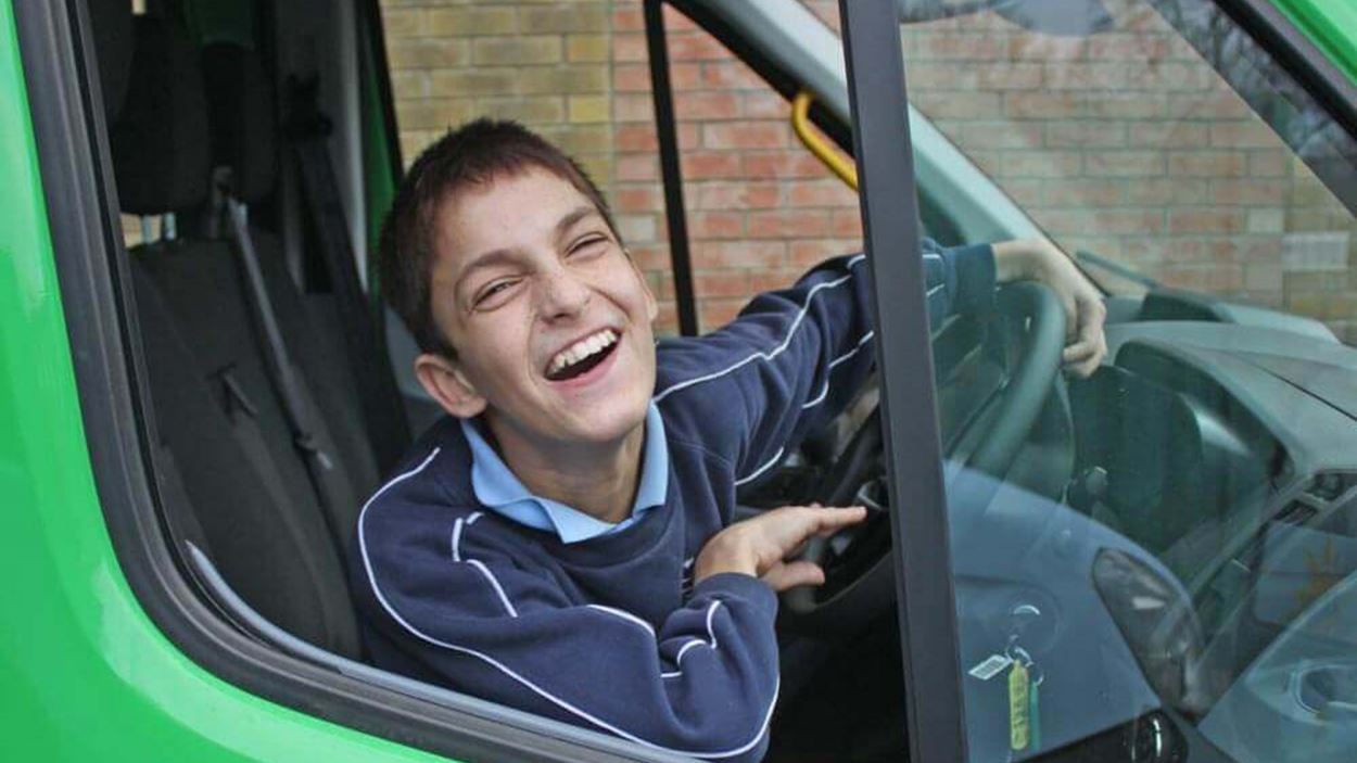 Little boy leaning out and laughing behind the wheel of a minibus