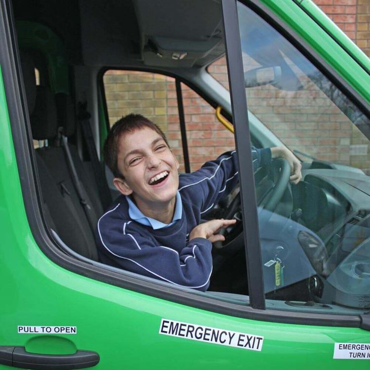 Little boy leaning out and laughing behind the wheel of a minibus