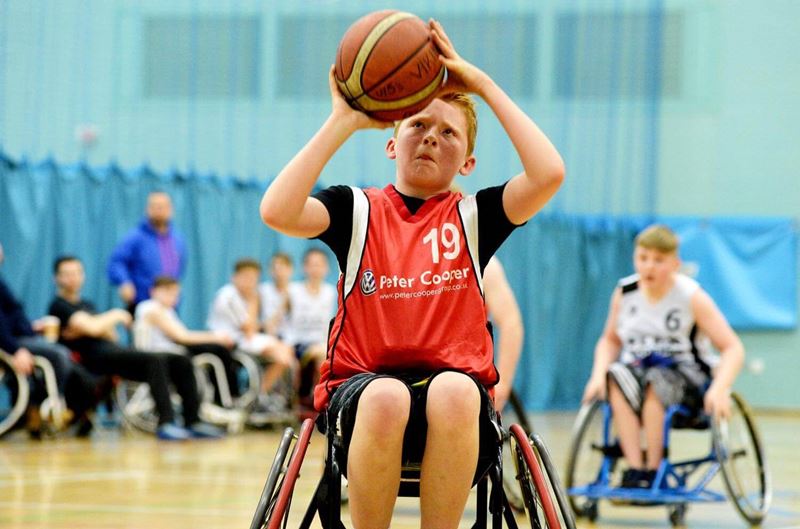 Young boy aiming to shoot the ball into the hoop in wheelchair basketball tournament