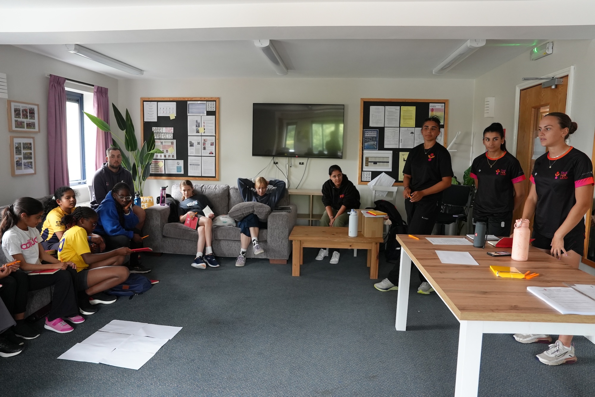 Classroom setting with girls sat on sofas around the edge of the room with worksheets and Take Her Lead Champions delivering a workshop from the other end of the room.JPG