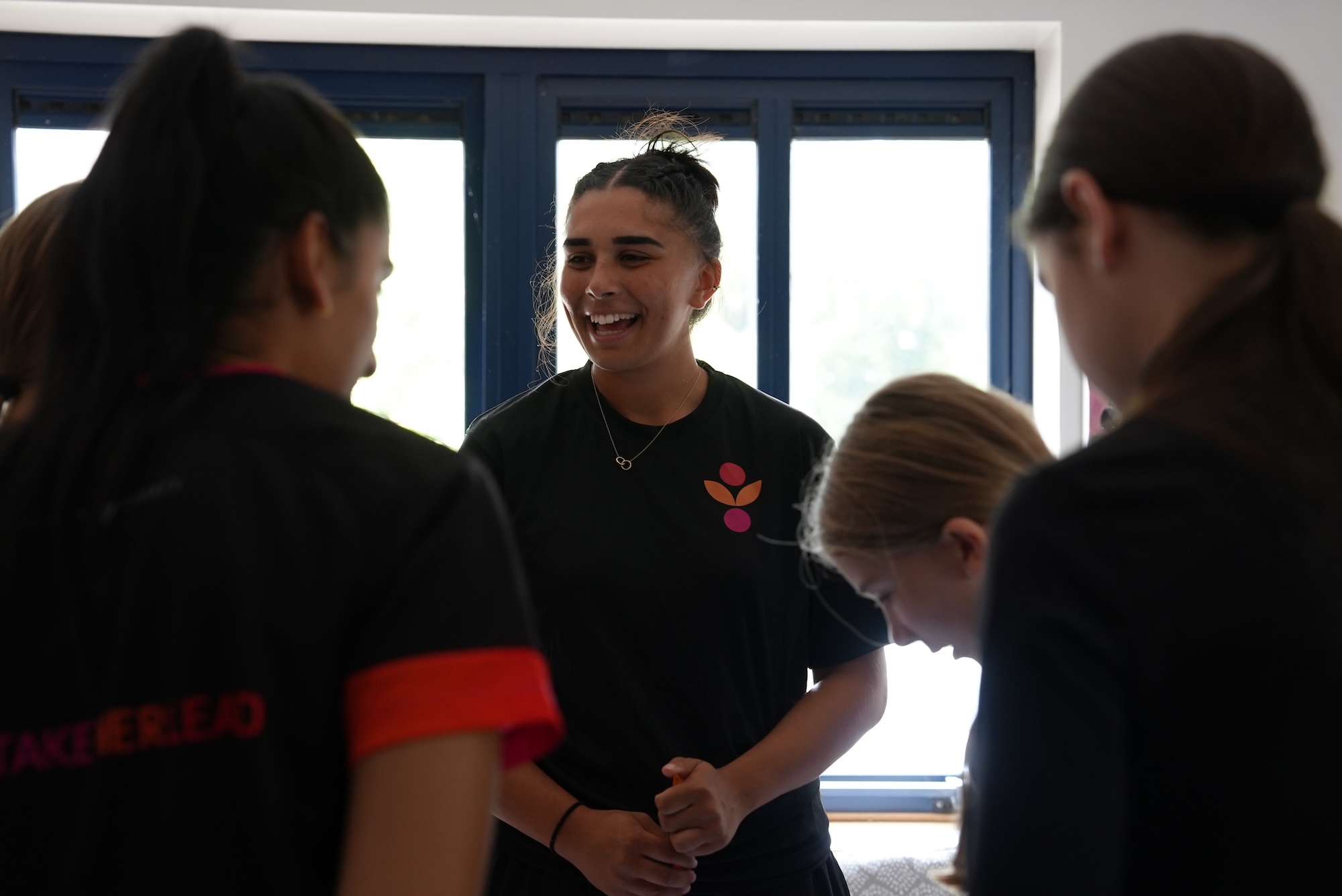 Group of Take Her Lead Champions and girl participants in a small group with one Champion laughing in the middle.JPG