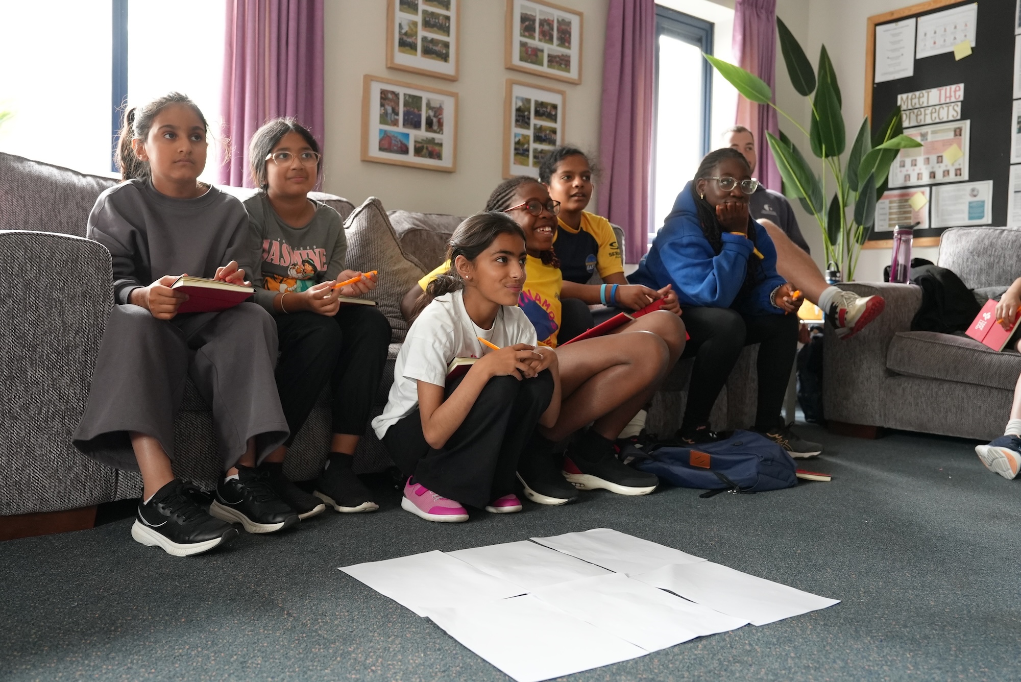 Group of girls sat on a sofa and some crouched on the floor listening intently to a Take Her Lead workshop being delivered with a worksheet on the floor in front of them.JPG