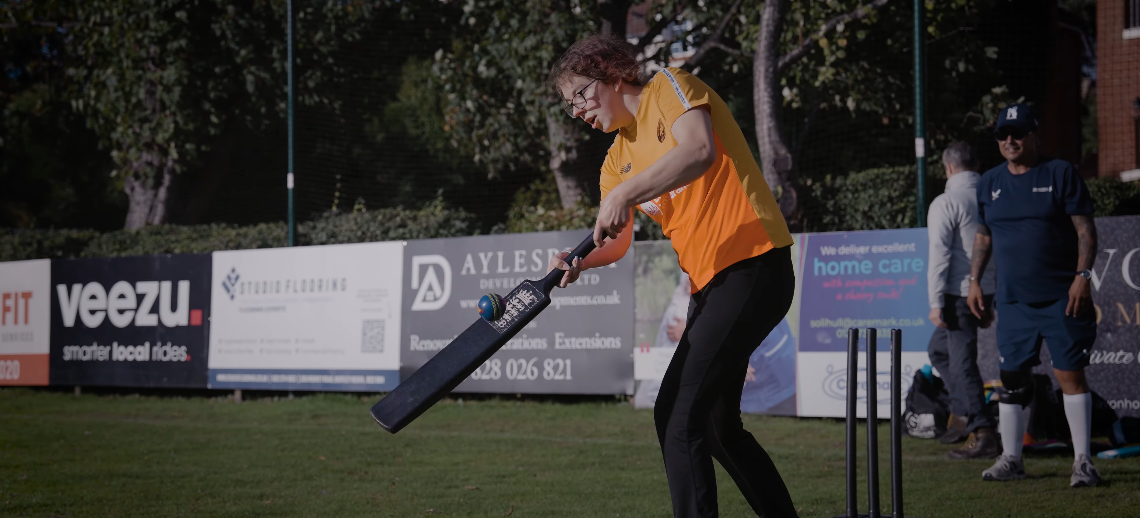 Millie hitting a cricket ball with a bat wearing a Birmingham Phoenix tshirt.png